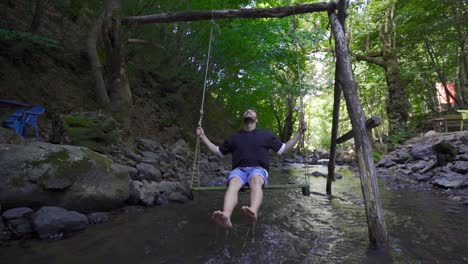 Young-man-swinging-on-a-swing-above-the-water.-Slow-Motion.